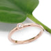 14kt rose gold bezel set diamond ring beside a green leaf