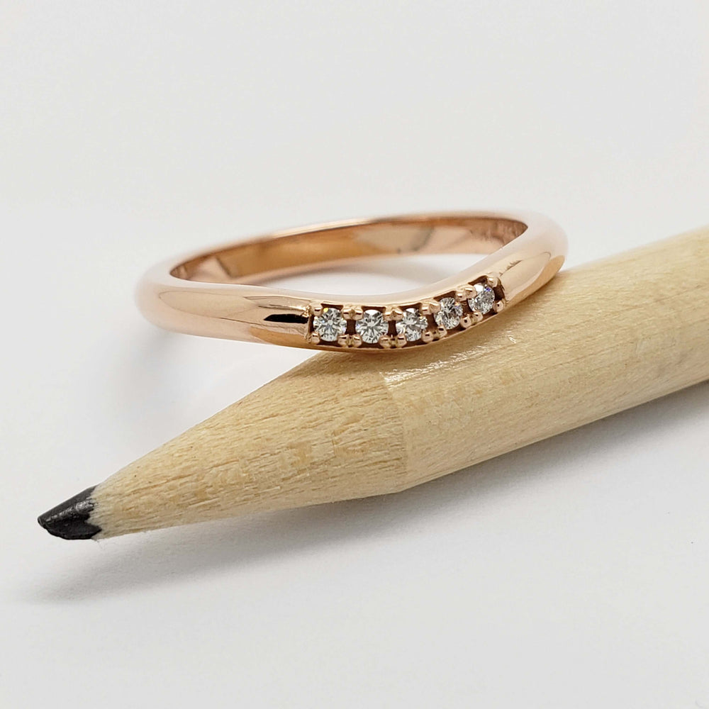 Rose gold chevron diamond wedding ring resting on a pencil