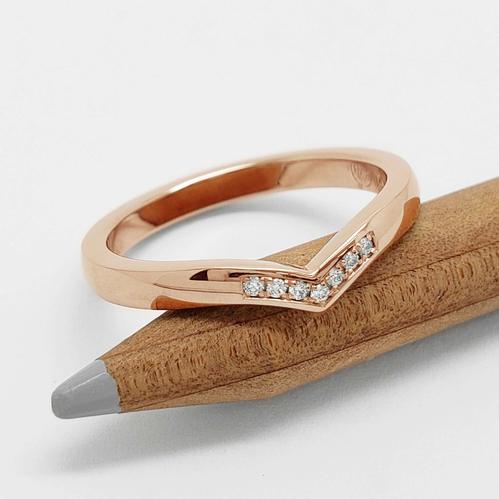 Rose gold chevron diamond wedding ring resting on a wooden pencil