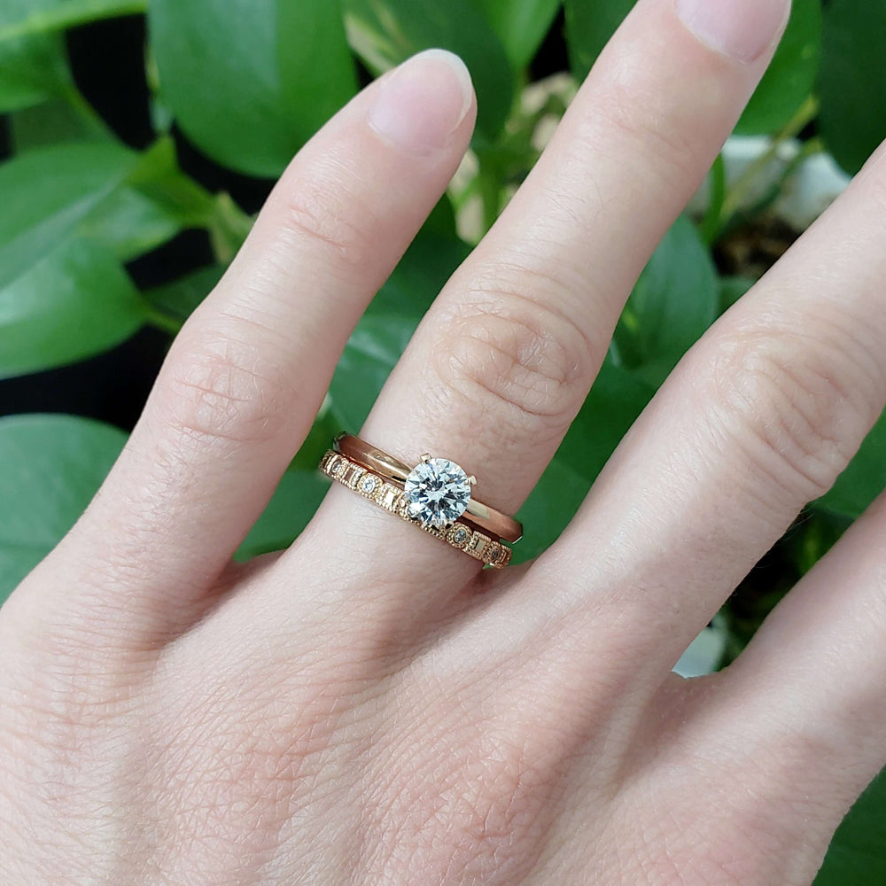Rose gold diamond wedding band stacked with solitaire engagement ring on hand