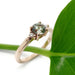 Rose gold engagement ring with green sapphire and diamonds, displayed on a green leaf