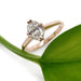 14kt rose gold engagement ring with oval lab diamond beside a green leaf