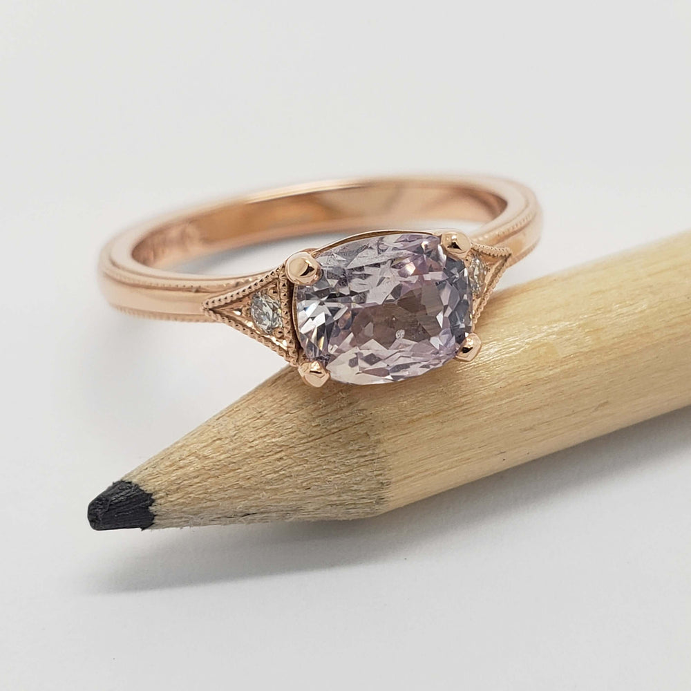 Rose gold ring with cushion cut pink sapphire and diamond accents on a pencil