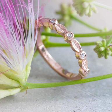 Rose gold wedding ring with diamond and leaf motif beside pink and green flowers