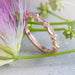 Rose gold wedding ring with diamond and leaf motif beside pink and green flowers