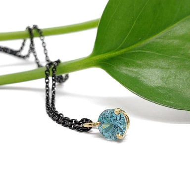 Round blue zircon pendant in 14kt yellow gold on black chain, styled with green leaf