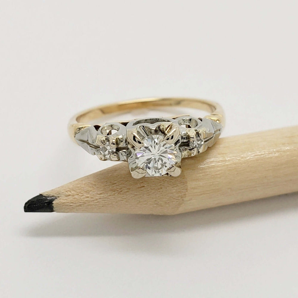 Round diamond two-tone engagement ring resting on a pencil for scale