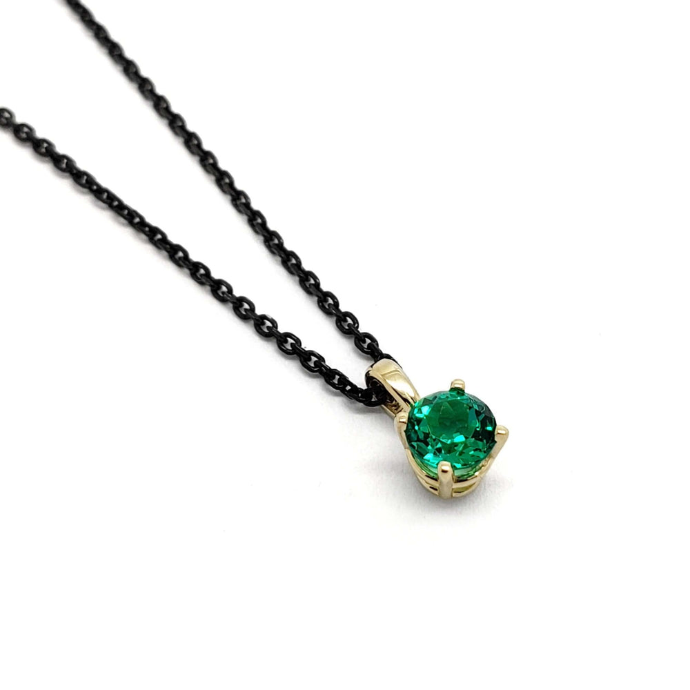Round lab-grown emerald pendant in 14kt yellow gold on a black chain, angled view