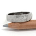 Rugged 14kt white gold wedding ring with hand carved facets, resting on a pencil