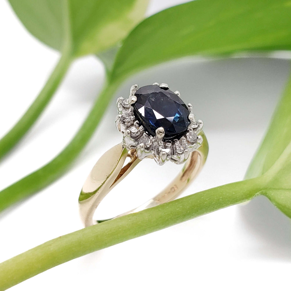 Sapphire and diamond halo ring in yellow and white gold with green leaves background