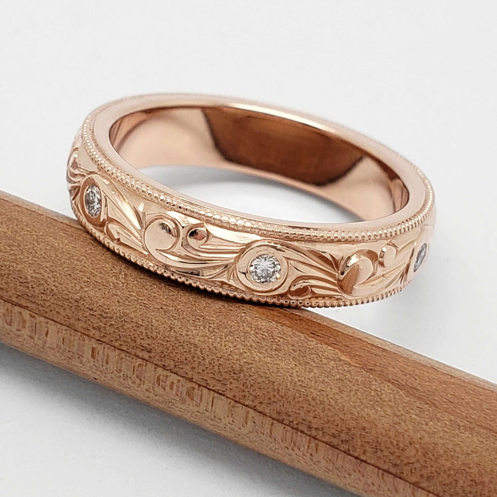 Scroll engraved rose gold wedding ring with diamonds, displayed on a pencil