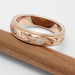 Scroll engraved rose gold wedding ring with diamonds, displayed on a pencil