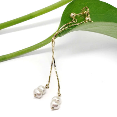 14kt yellow gold seed pearl dangle earrings displayed on a green leaf