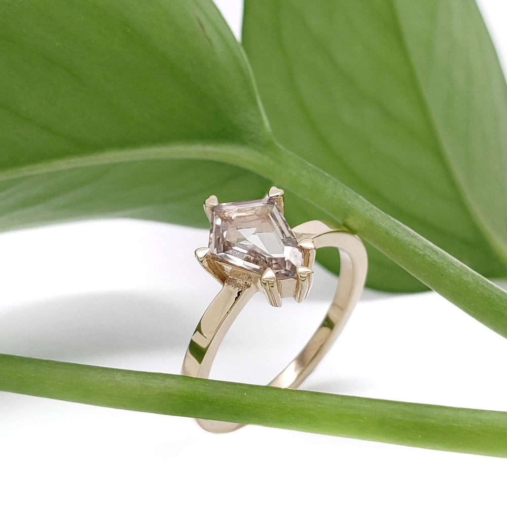 Shield cut grey sapphire engagement ring in yellow gold, displayed on green leaves