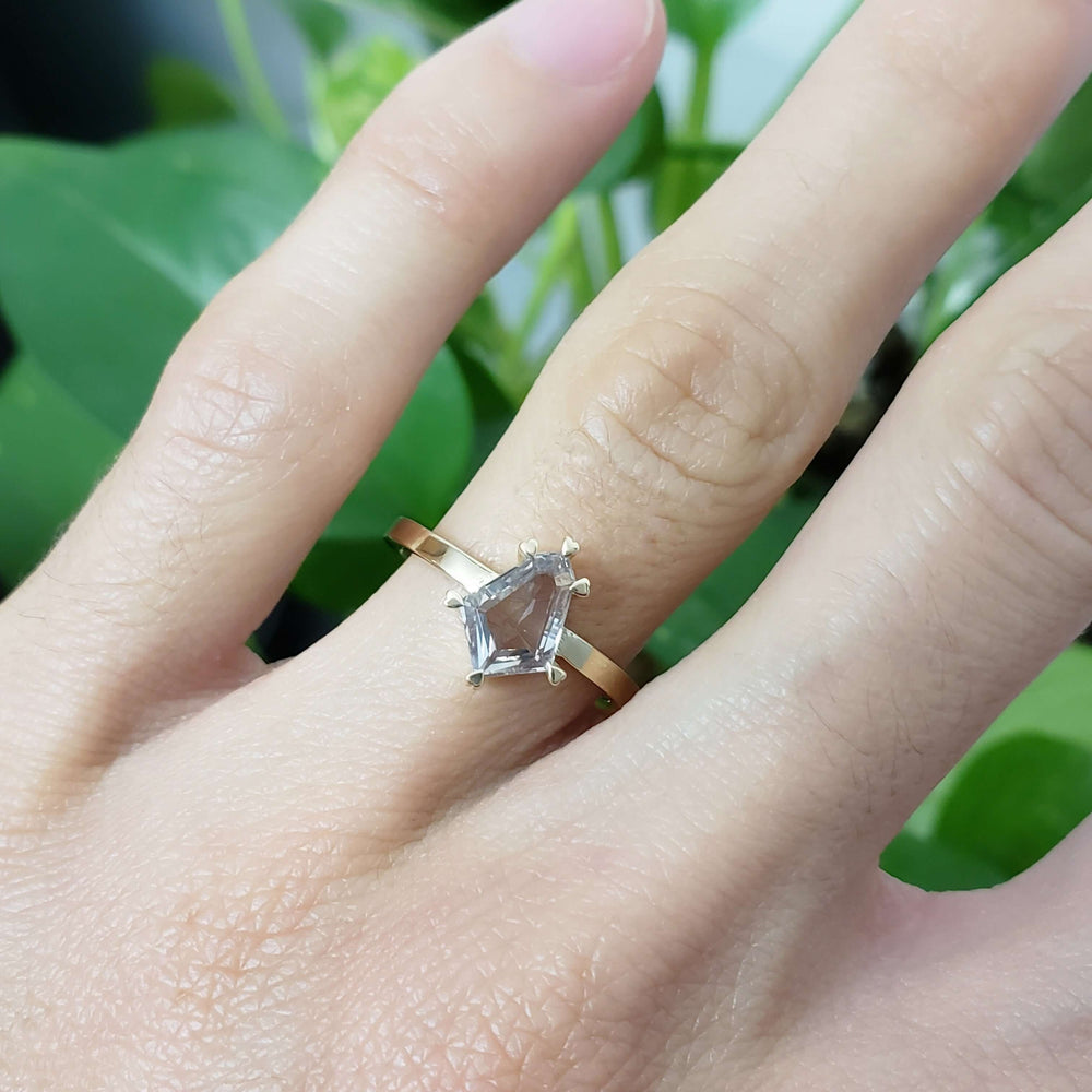 Shield cut grey sapphire engagement ring in yellow gold, worn on a hand