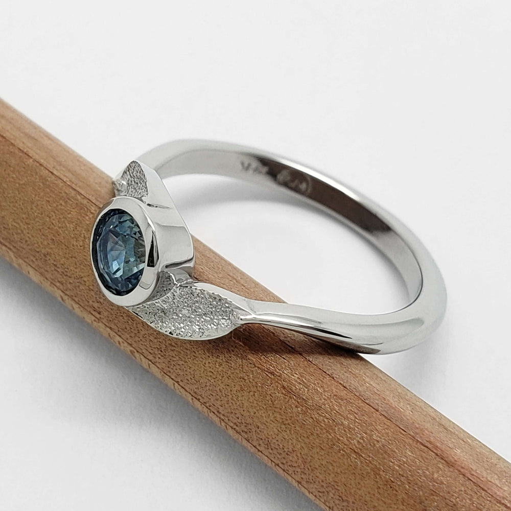 Side view of white gold Montana sapphire leaf ring on a pencil