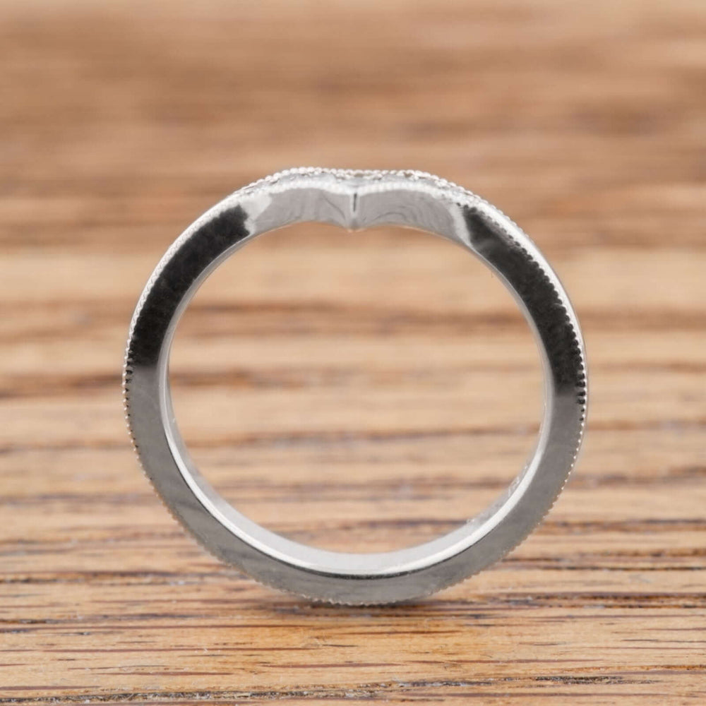 Side profile of 14k white gold chevron wedding band with millgrain edge on wood surface