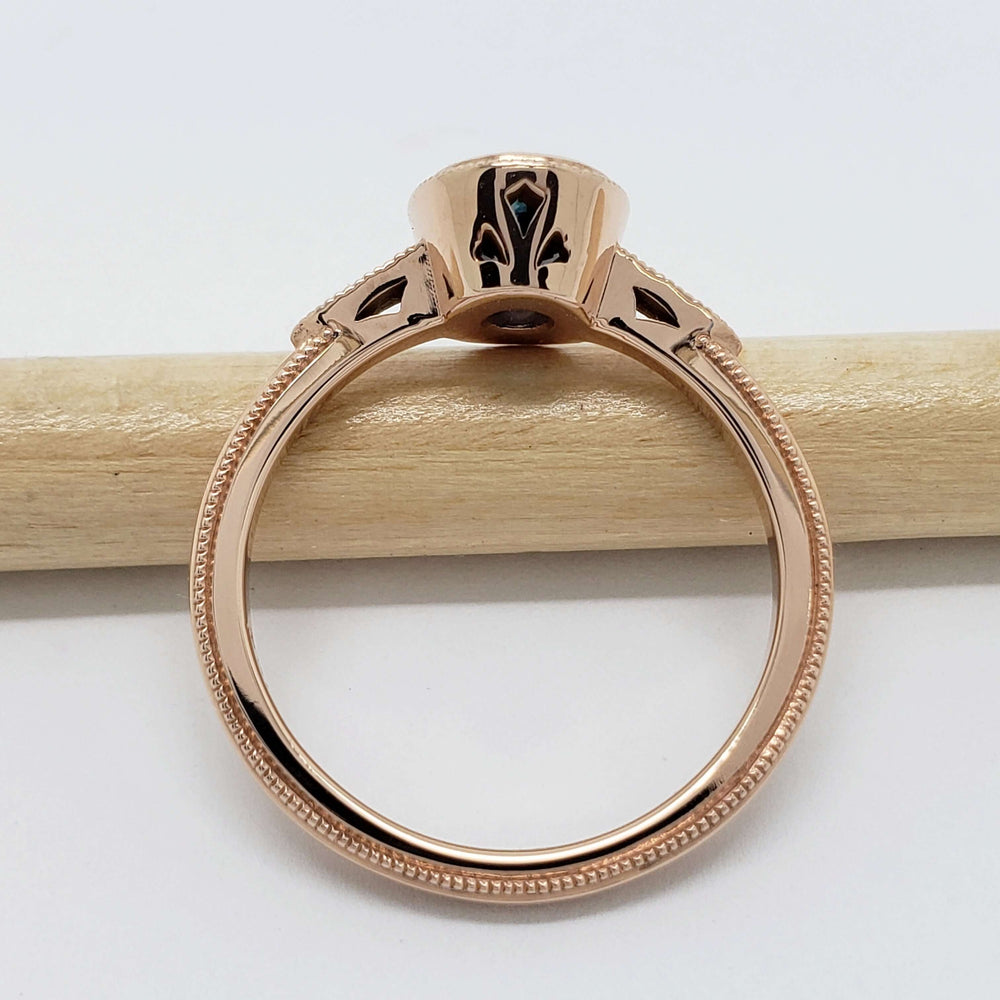 Side view of 14kt rose gold ring with cutout gallery and millgrain details, shown on a pencil
