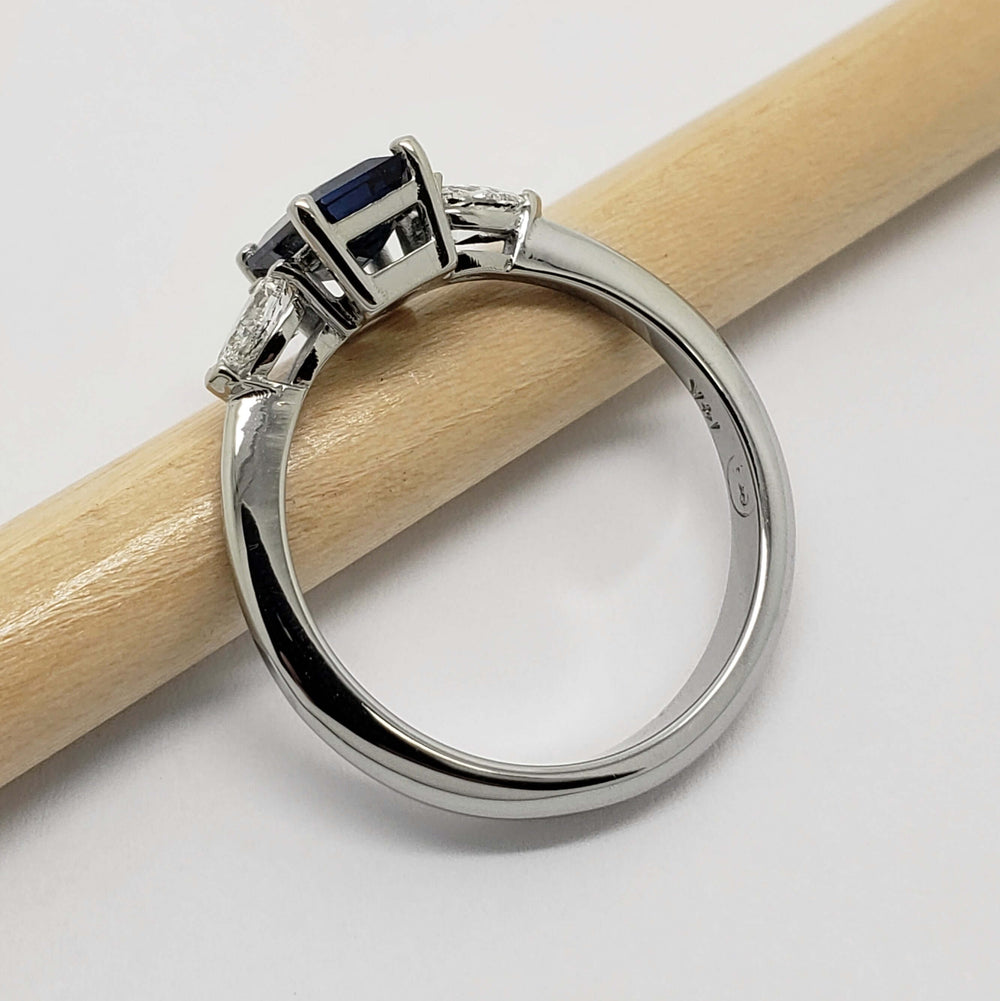 Side profile of 14kt white gold ring with blue emerald cut sapphire and pear diamonds