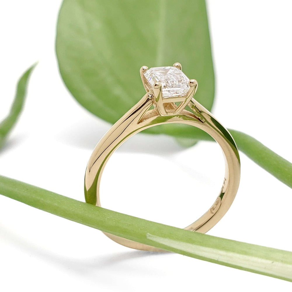 Side view of 14kt yellow gold emerald cut lab diamond ring with plant background