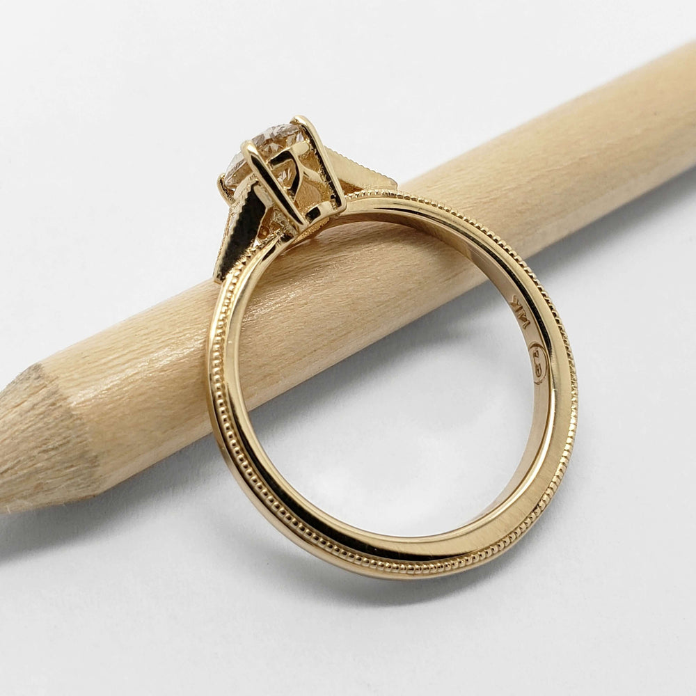 Side view of 14kt yellow gold engagement ring with millgrain and champagne diamond, on a pencil