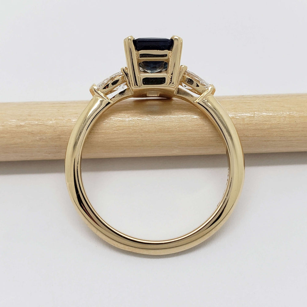 Side profile of 14kt yellow gold ring with blue sapphire and lab diamonds, resting on a pencil