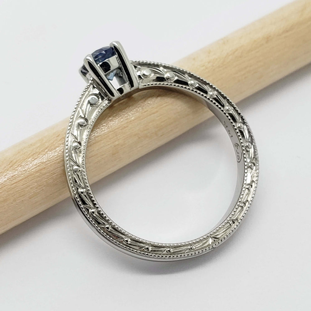 Side view of engraved white gold ring with blue Montana sapphire and diamond accents on a pencil
