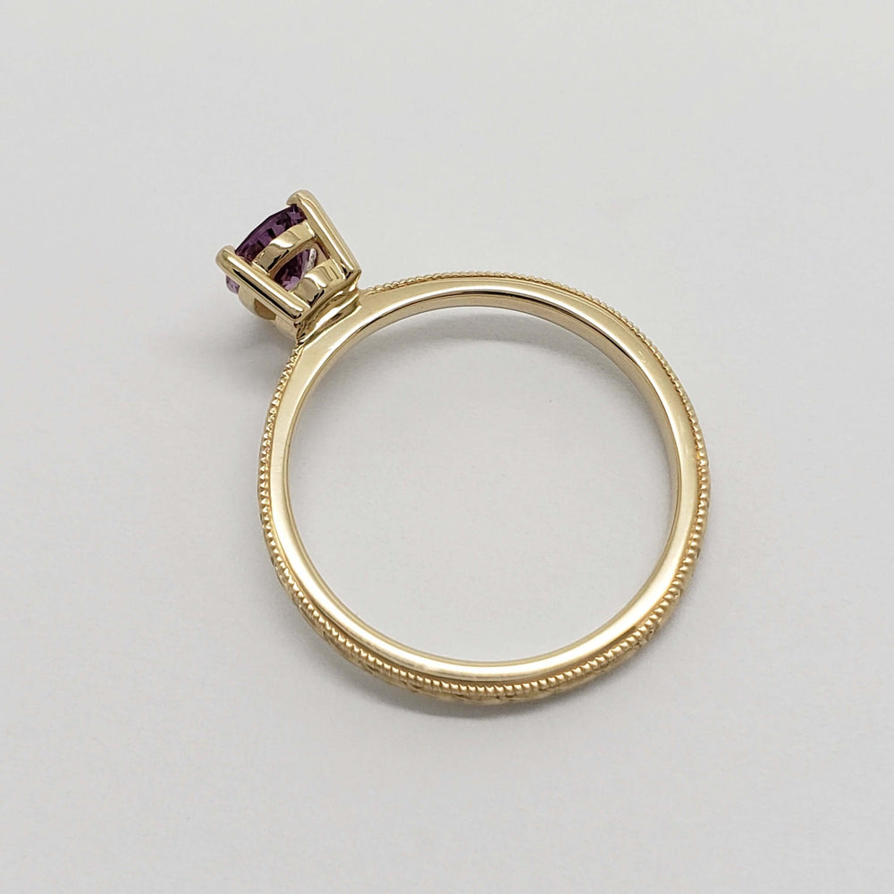 Side profile of engraved yellow gold ring with pink sapphire center stone