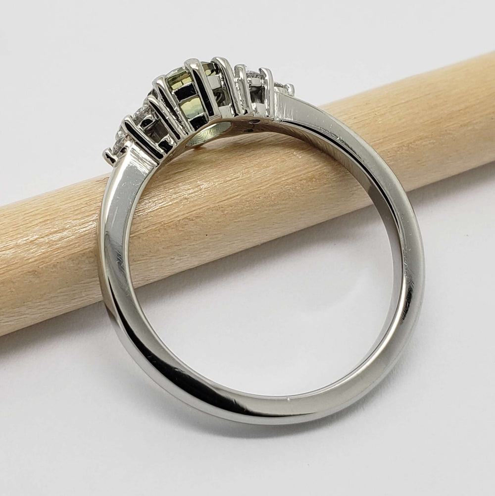Side profile of 14k white gold ring with green sapphire and diamonds, beside a pencil