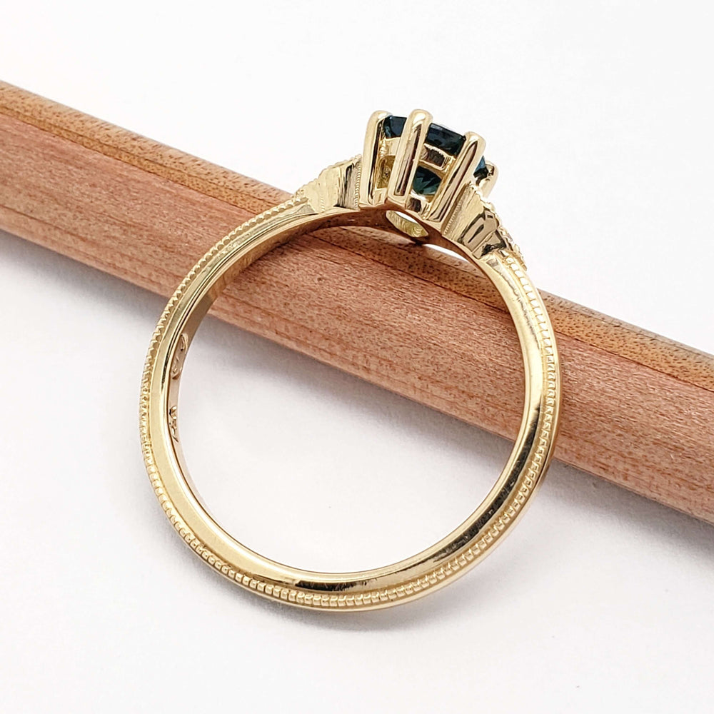 Side profile of yellow gold Montana sapphire and diamond engagement ring with millgrain detail