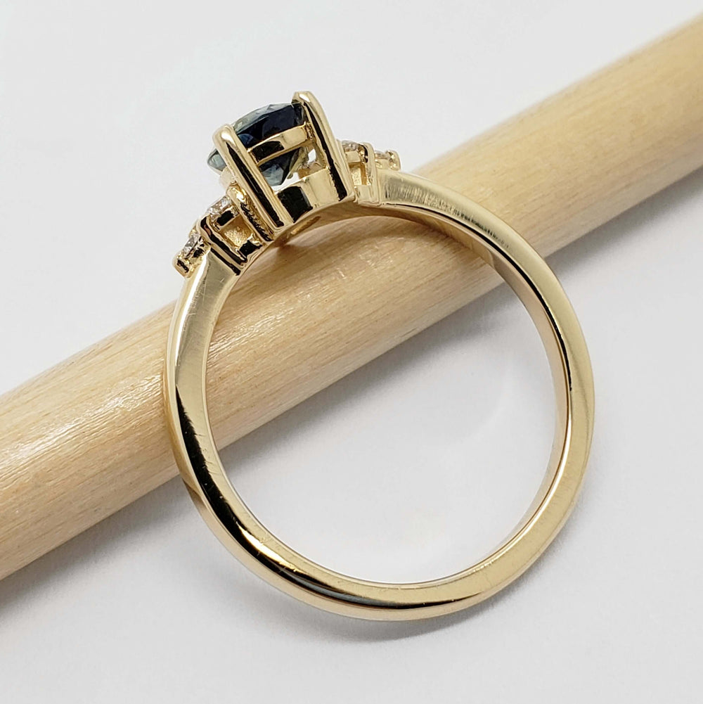 Side view of 14k yellow gold ring with blue sapphire and diamond accents, on a pencil