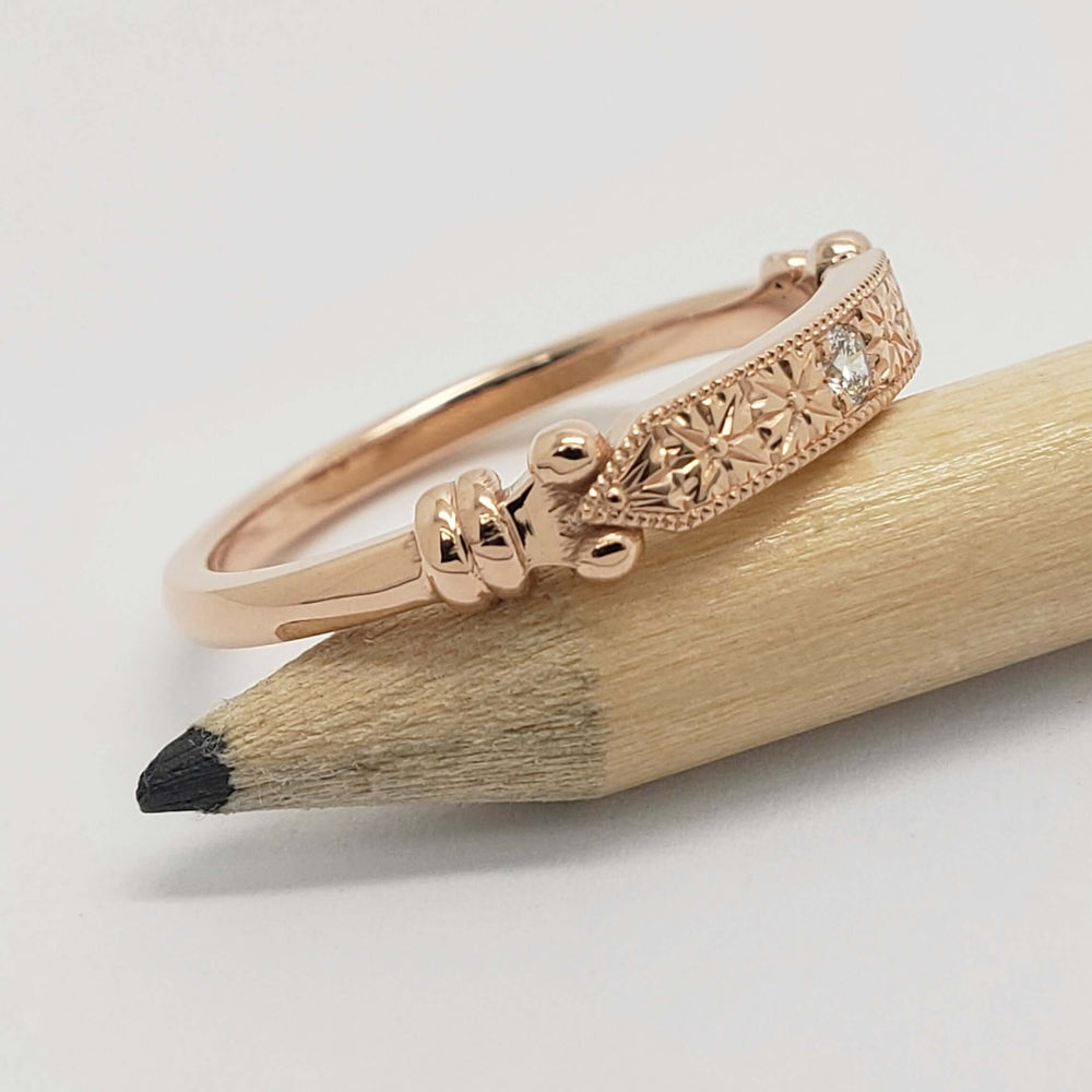 Side view of 14kt rose gold engraved wedding ring with lab diamond, resting on a pencil