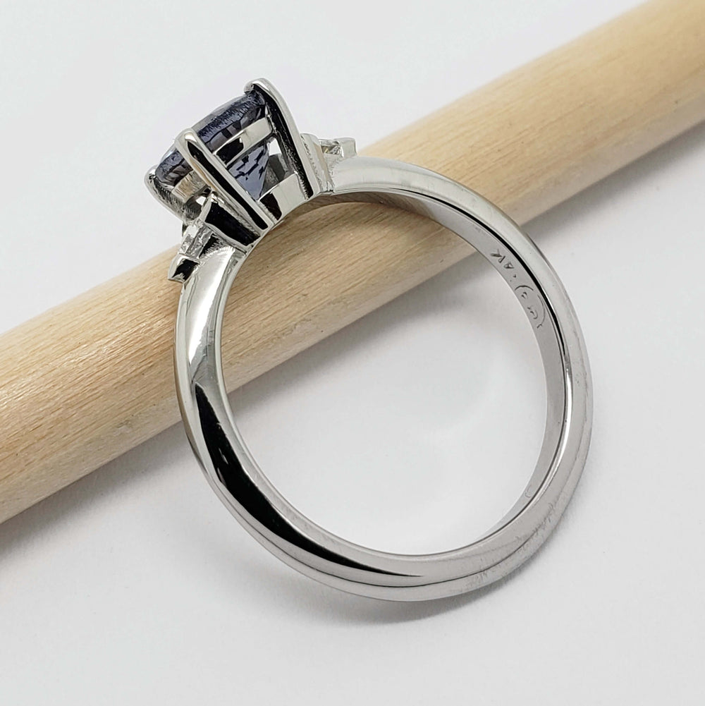 Side view of 14kt white gold ring with blue-grey spinel and triangle diamonds on a pencil