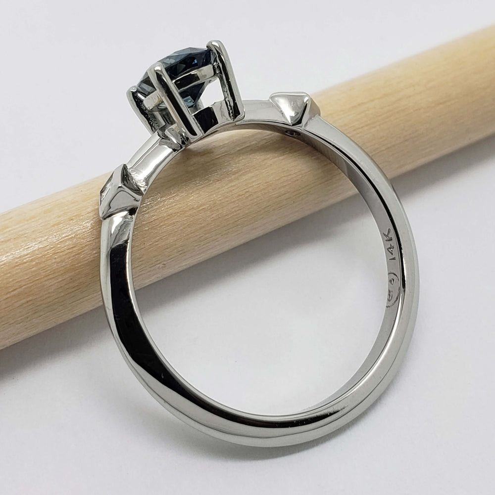 Side view of 14kt white gold ring with sapphire and diamond accents on a pencil