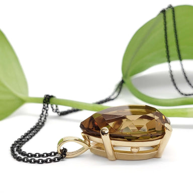 Side profile of 14kt yellow gold pear citrine pendant with black chain and green leaf