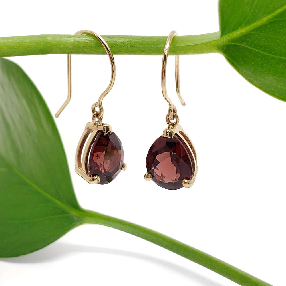 Side view of pear garnet drop earrings in 14kt yellow gold hanging from a green stem