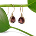 Side view of pear garnet drop earrings in 14kt yellow gold hanging from a green stem