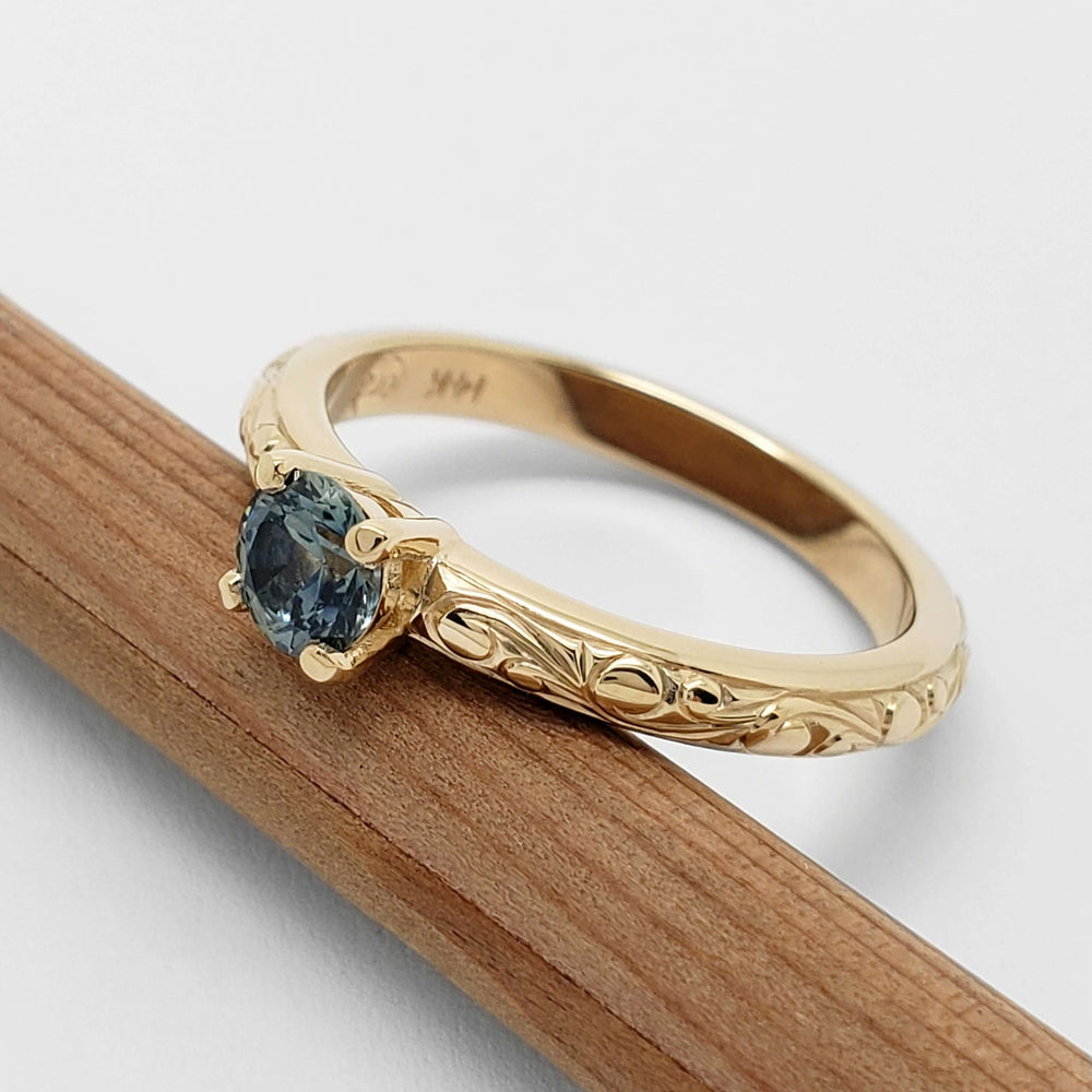 Side view of 14kt yellow gold ring with blue Montana sapphire and detailed hand engraving
