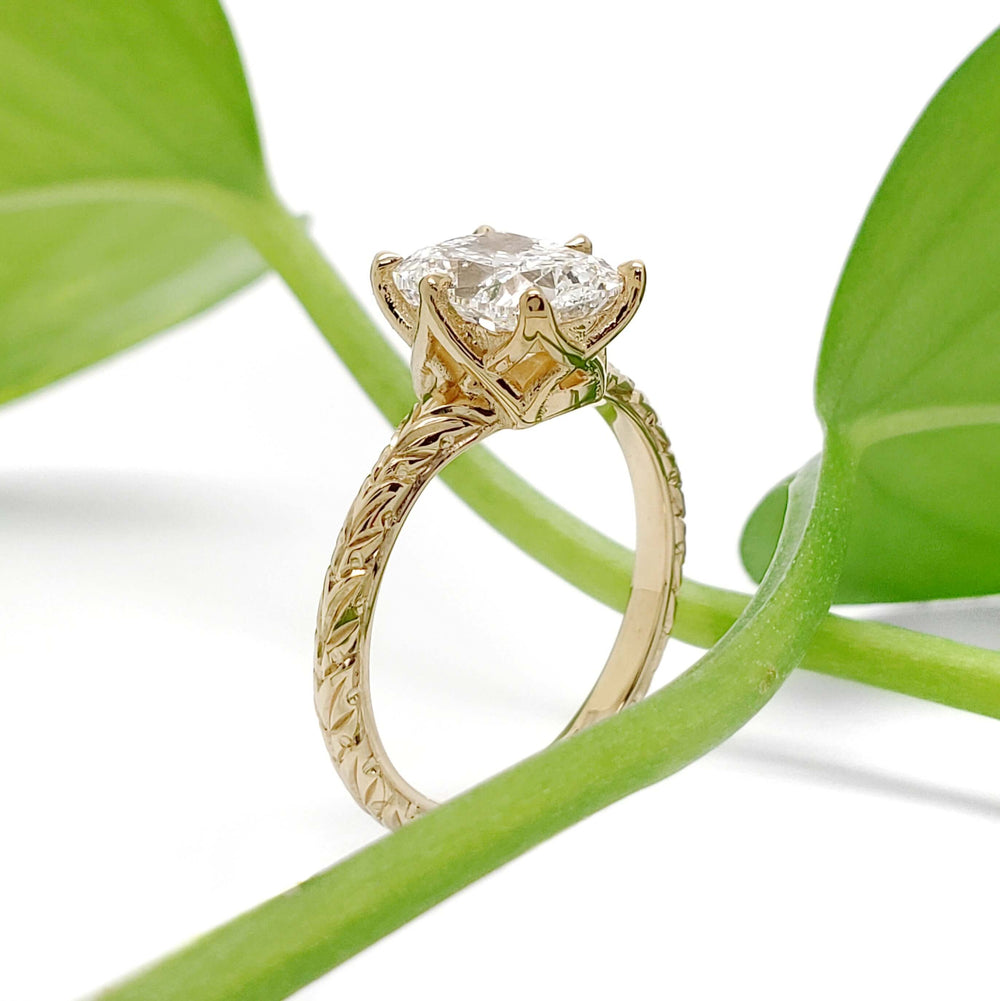Side view of 14kt yellow gold ring with cushion cut lab diamond, leaf engraving, and plant background