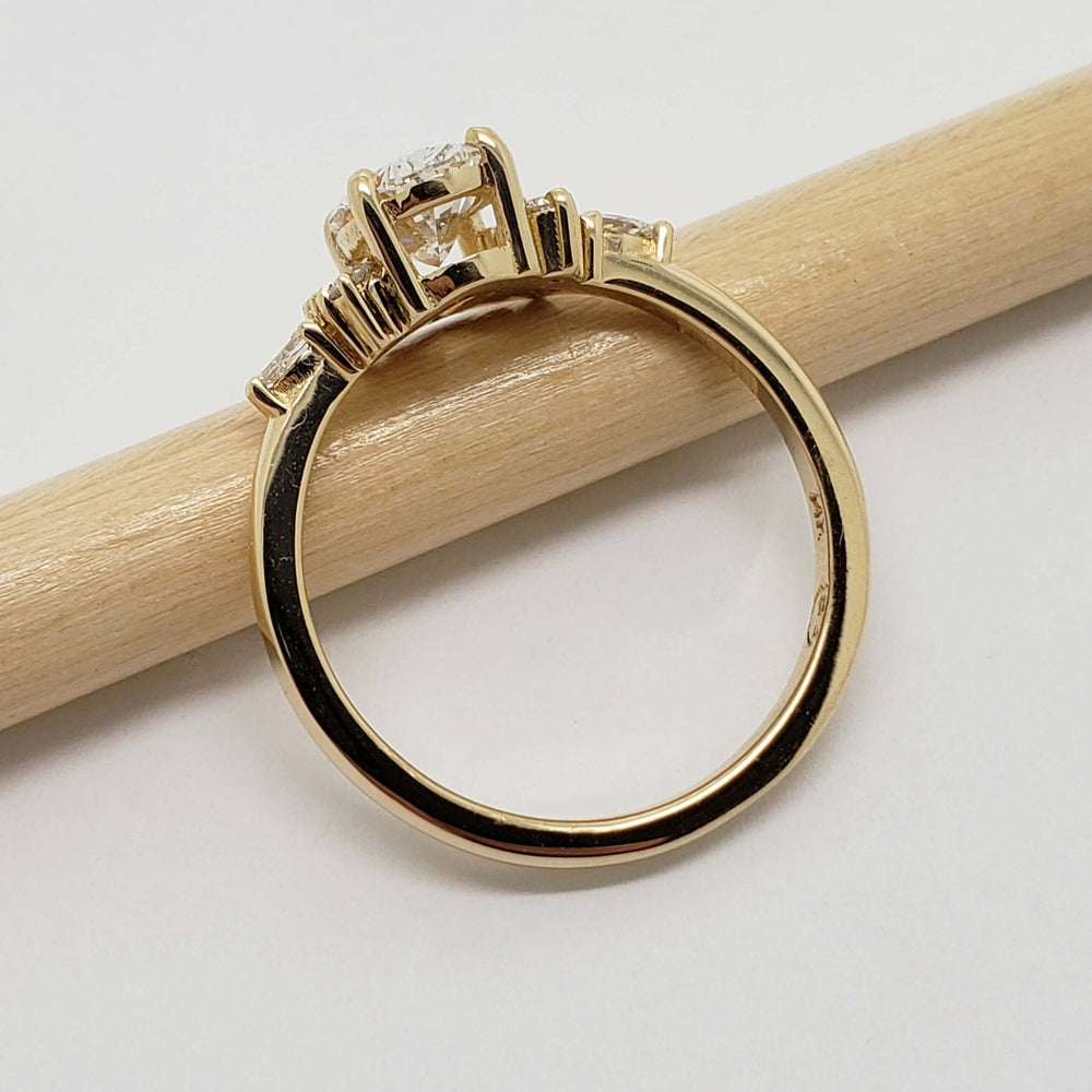 Side profile of 14kt yellow gold cluster engagement ring with oval lab diamond on a pencil