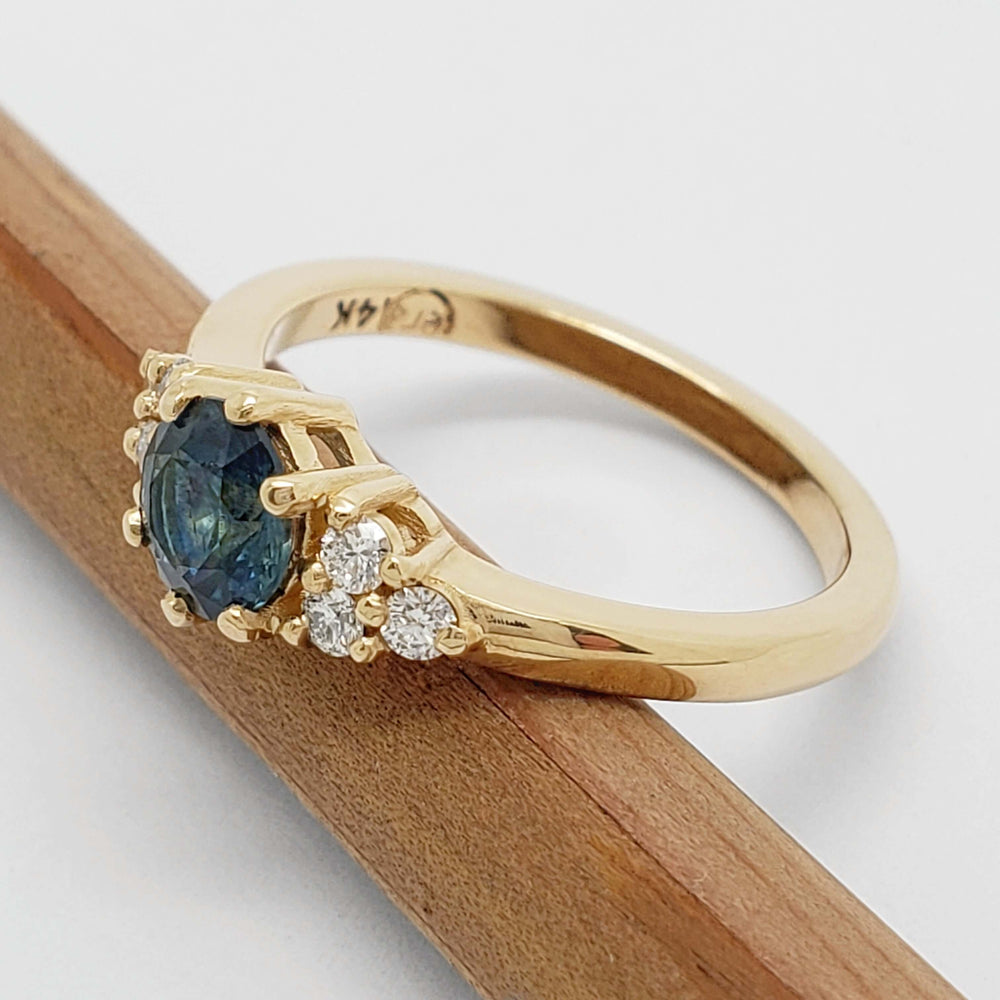 Side view of 14k yellow gold ring with blue Montana sapphire and diamonds on a pencil