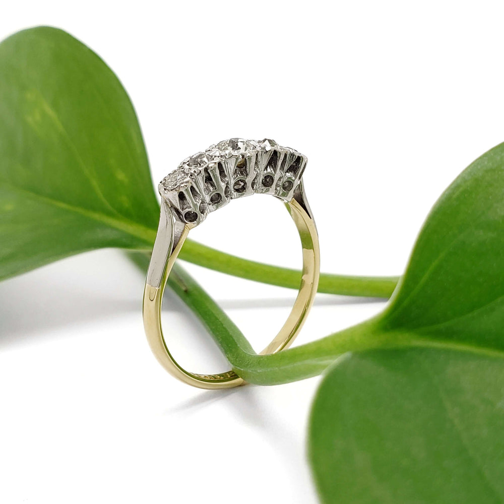 Side view of antique five-stone diamond ring with yellow gold band and platinum setting, against green leaves
