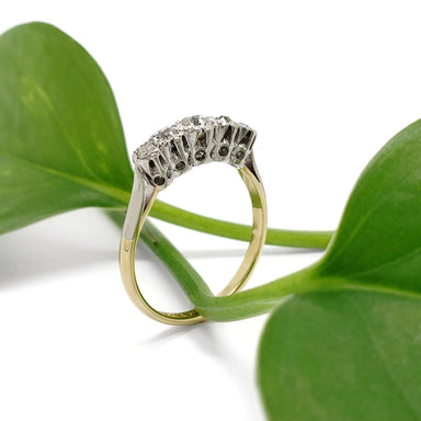 Side view of antique five-stone diamond ring with yellow gold band and platinum setting, against green leaves