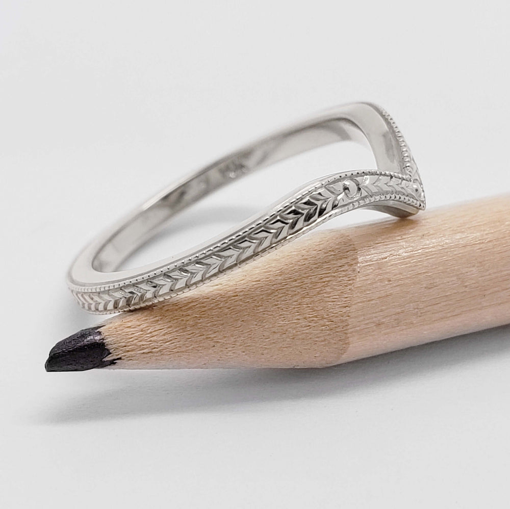 Side view of engraved 14kt white gold chevron wedding ring resting on a pencil