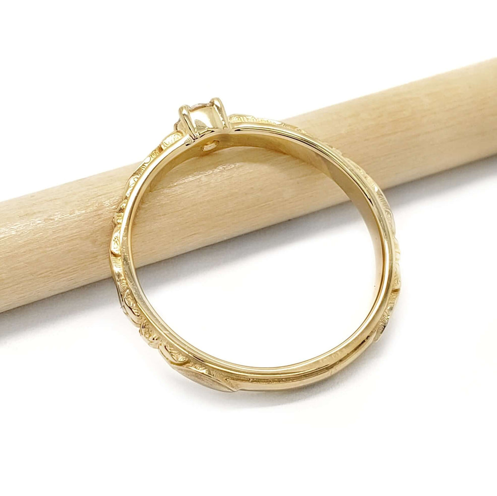 Side view of 14kt yellow gold engagement ring with engraved band resting on a pencil