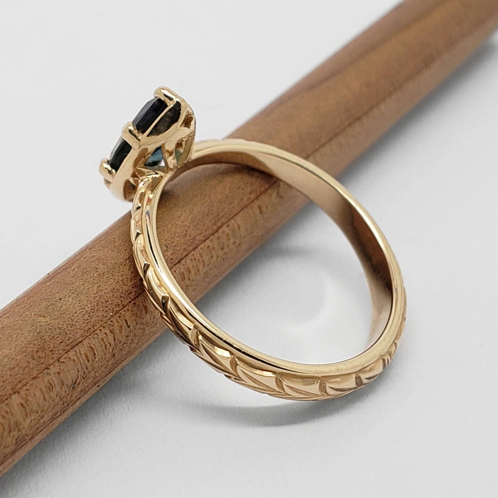 Side view of engraved 14kt yellow gold ring with marquise green sapphire setting