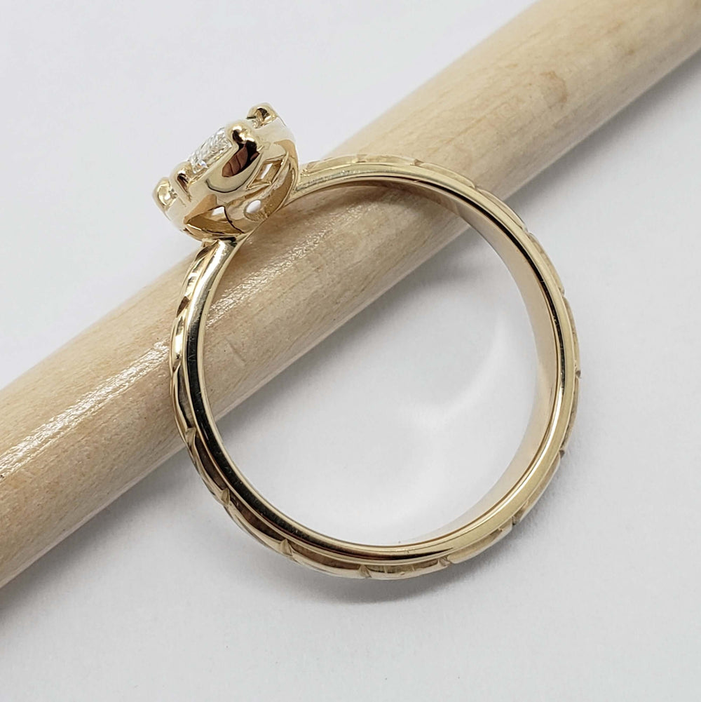 Side view of engraved 14kt yellow gold ring with marquise lab diamond, displayed on pencil