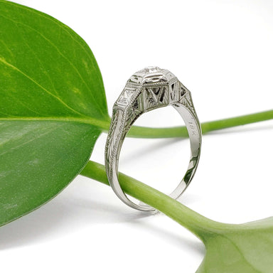 Side view of engraved 18kt white gold hexagon-set diamond ring resting on a green leaf