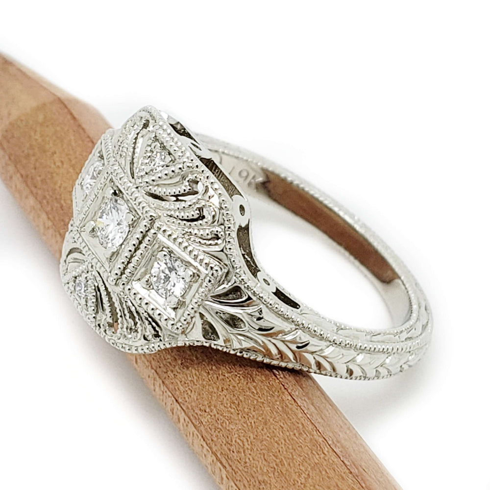 Side view of engraved 19kt white gold Art Deco diamond ring resting on a wooden stick