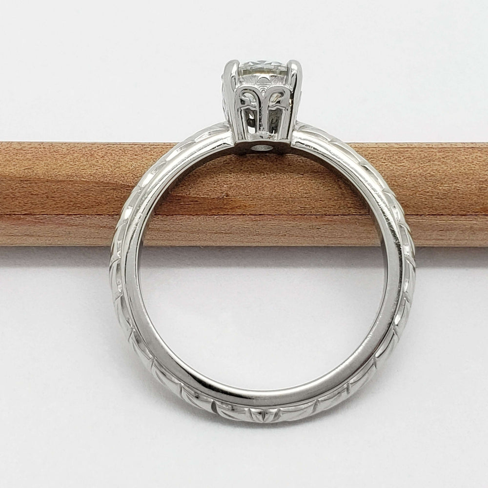 Side view of engraved 14kt white gold moissanite ring on a pencil